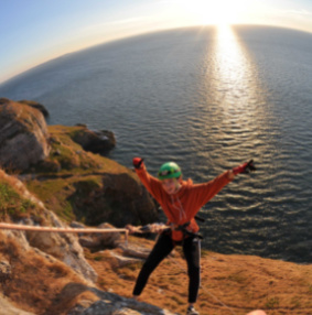 Girl abseiling with sea and sun in background